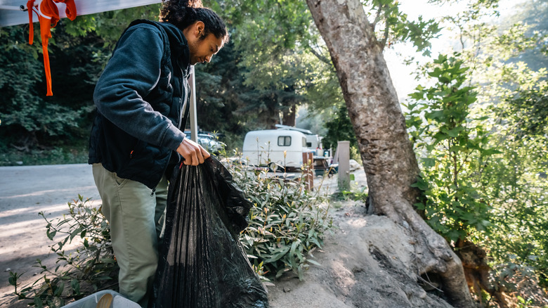 A camper at a campsite picking up trash and placing it in a trash bag