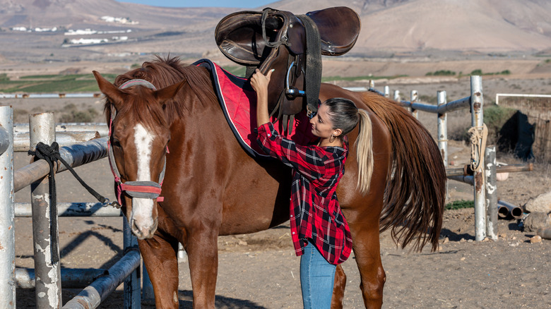 A person placing a saddle on a horse