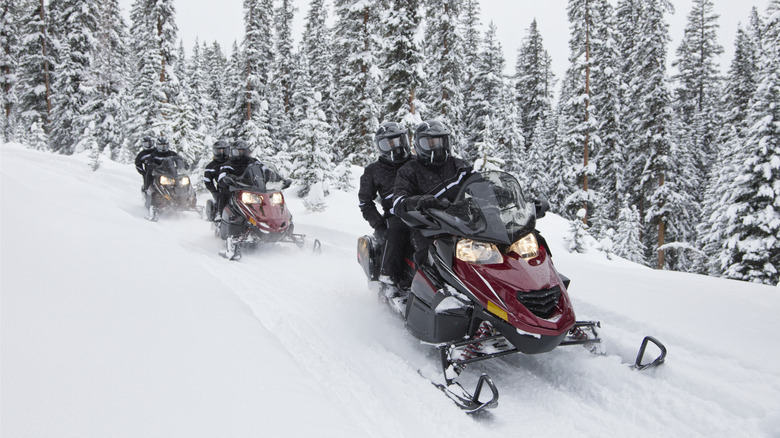 Three pairs of people riding down mountain on snowmobiles