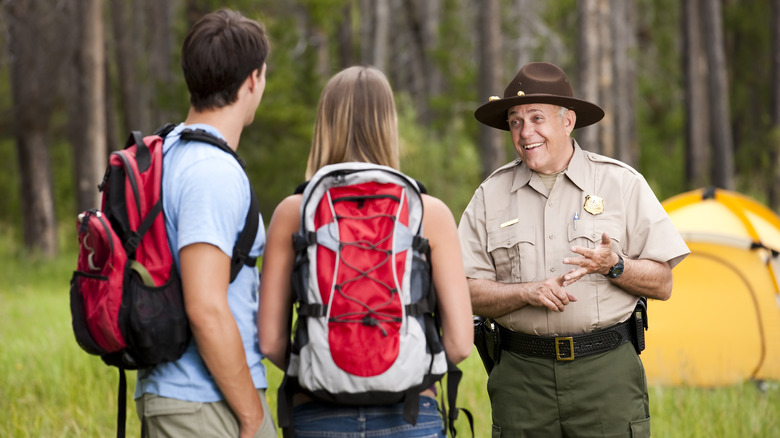 Man and woman with backpacks speaking to happy park ranger