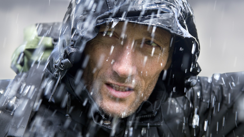 Man wearing hooded coat grimacing in the rain 