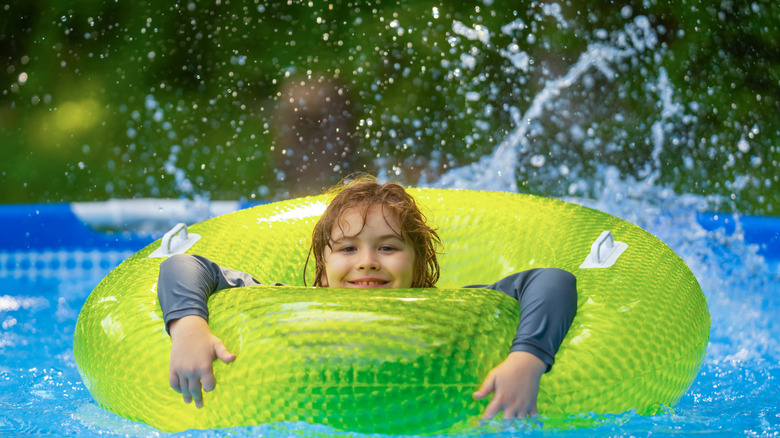 Child splashing through an above-ground pool with a green inner tube and water splashing everywhere