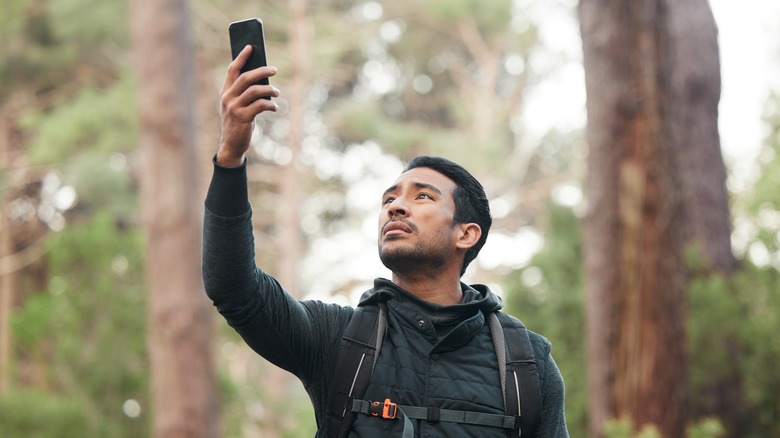 Worried hiker in woods holding phone up high