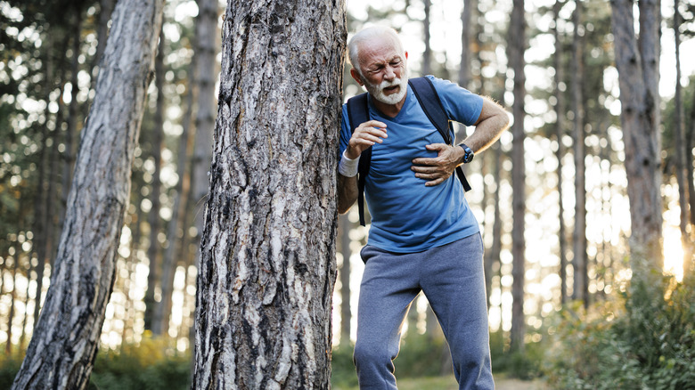 Hiking man clutching his chest, leaning against tree