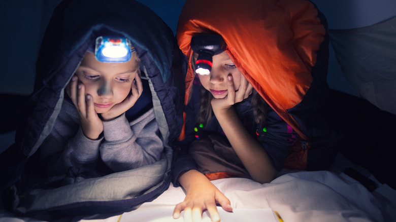 Kids reading by flashlight in tent