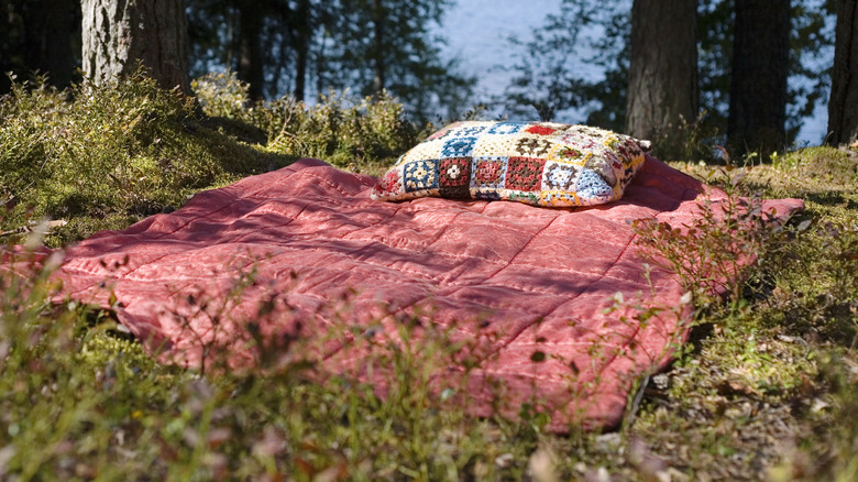 A crocheted pillow on top of a sleeping back out in the wilderness