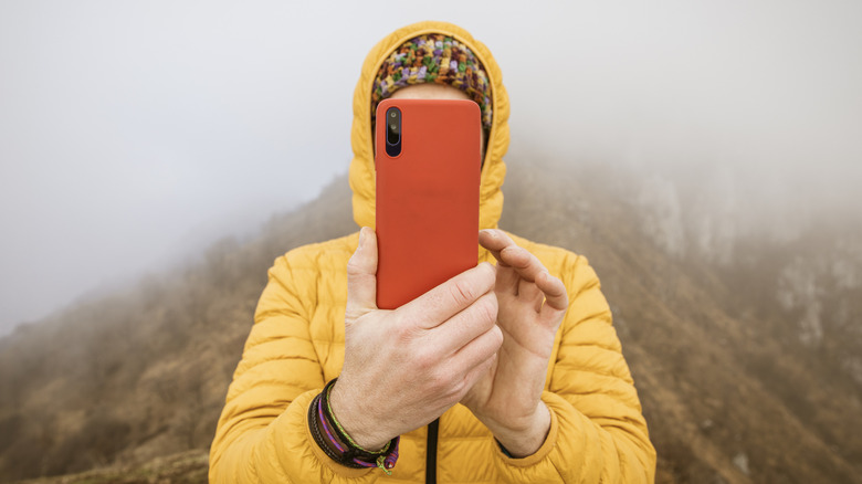 Man with hood, taking photo with iPhone outside on mountain