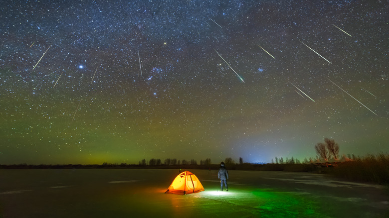 Person standing next to lit up tent in field during meteor shower 