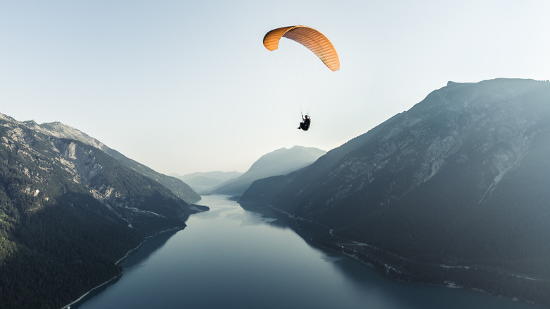 Paraglider soaring over water between mountains