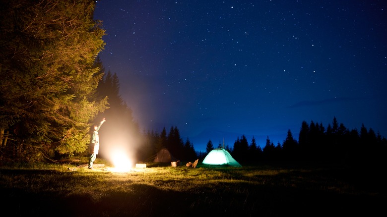 Camper standing near tent pointing up at night sky