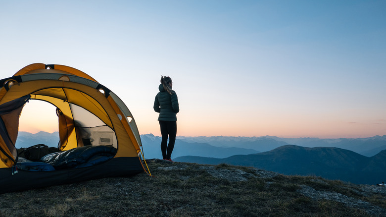Solo female camper standing in front of tent looking out