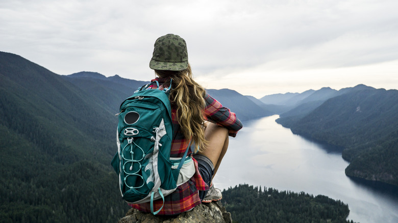 Woman seated on cliff overlooking water, wearing backpack