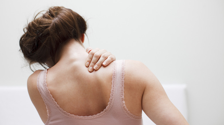 Back of woman hunched over rubbing her right shoulder blade