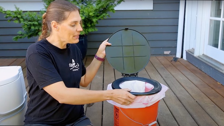 Woman lifting lid of bucket toilet