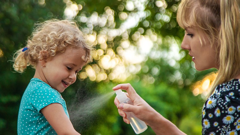 Woman spraying bug spray on child