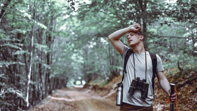 Male hiker with binoculars wiping sweat off brow