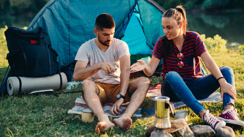 Couple sitting outside camping tent with supplies